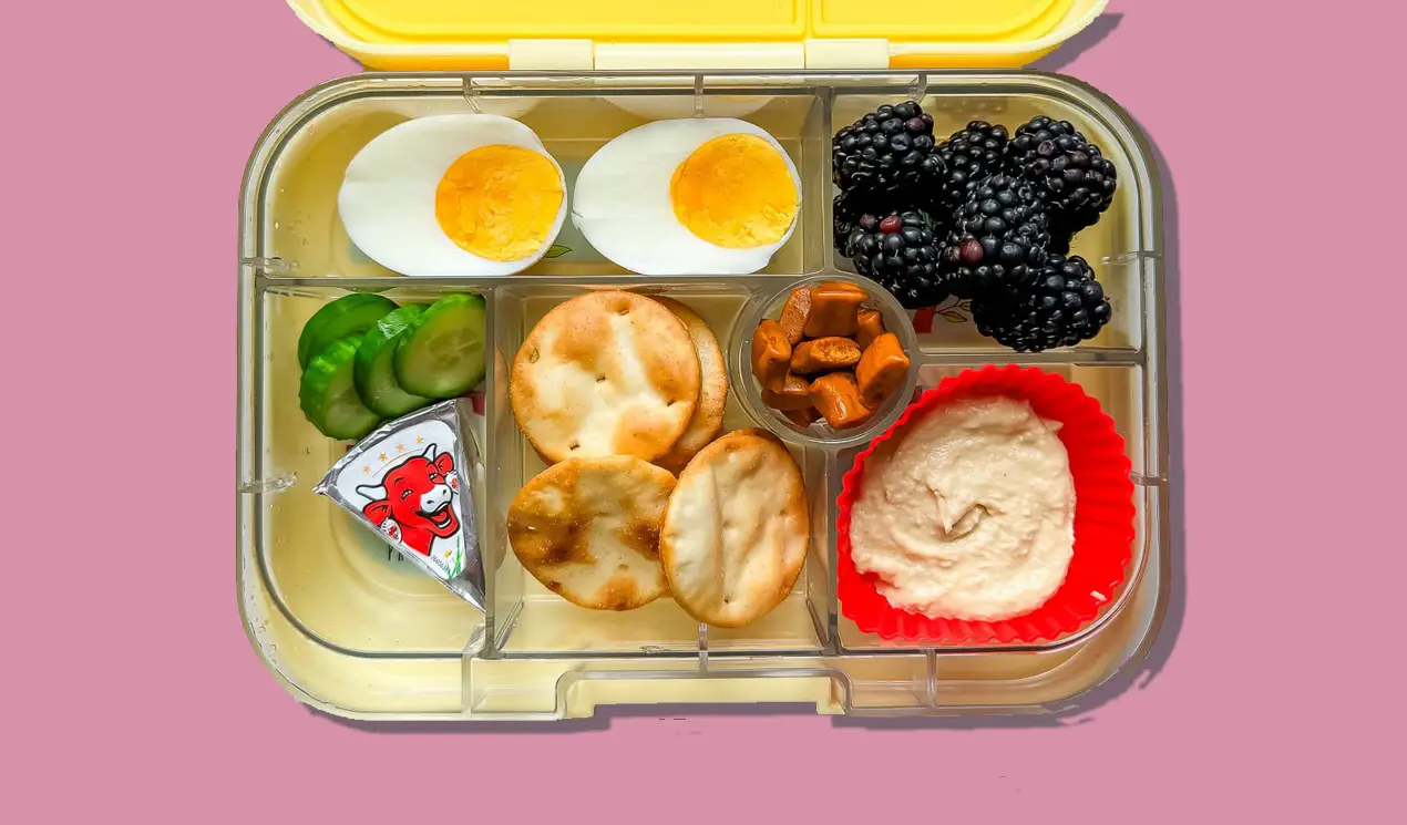 A lunch box with hummus with pita crackers, Laughing Cow cheese wedge, cucumber slices, hard boiled egg, blackberries and Soley Gummies. A lunch box with hummus with pita crackers, Laughing Cow cheese wedge, cucumber slices, hard boiled egg, blackberries and Soley Gummies.
