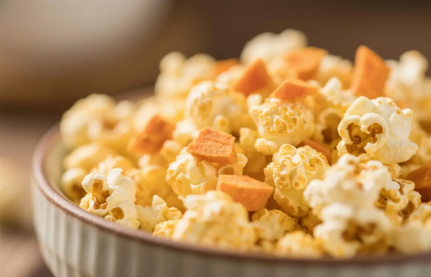 Cheddar-themed popcorn with cheddar cheese and butter slices, in a white bowl, close-up. The texture of the popcorn is visible, while large pieces of orange cheese and yellow butter, arranged around it, create an attractive visual appeal. The background has a soft focus on the color beige or light brown to emphasize the details of the snacks. Cheddar-themed popcorn with cheddar cheese and butter slices, in a white bowl, close-up. The texture of the popcorn is visible, while large pieces of orange cheese and yellow butter, arranged around it, create an attractive visual appeal. The background has a soft focus on the color beige or light brown to emphasize the details of the snacks.