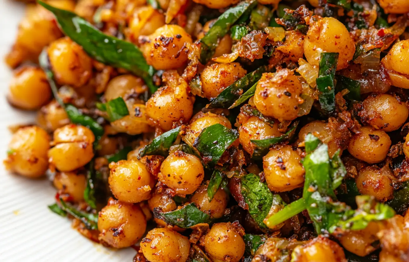 A close-up of the spiced chickpeas, showcasing their golden-brown texture and vibrant colors from fresh green herbs. The background is a simple white plate with visible details like tiny cracks in its surface, adding to the visual appeal. This composition captures the essence of an appetizing dish ready for serving. A close-up of the spiced chickpeas, showcasing their golden-brown texture and vibrant colors from fresh green herbs. The background is a simple white plate with visible details like tiny cracks in its surface, adding to the visual appeal. This composition captures the essence of an appetizing dish ready for serving.