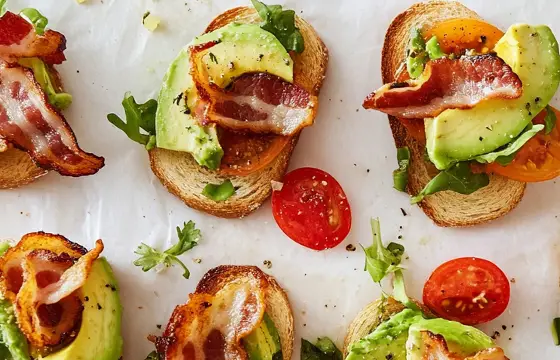 Compose the classic Cobb salad in an overhead shot of small toasts with avocado, bacon, and tomato slices, arranged on top of each other. The background is white paper, with soft lighting that highlights the textures of the bread and vegetables. A hand reaching out from off-screen takes one of the toasts to taste it, capturing its fresh texture and vibrant colors.